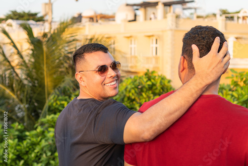 Latin Man affectionately placing hand on friend's head as they share a moment in golden hour light.