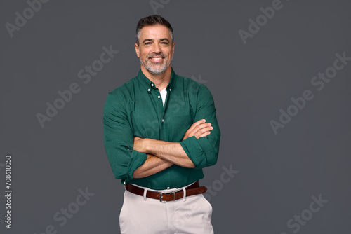 Portrait of elegant older business man, smiling middle aged mature businessman professional executive or lawyer wearing green shirt looking at camera standing arms crossed isolated on gray background.