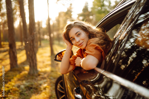 Young happy woman leaning out of the car window enjoying travel. The concept of active lifestyle, travel, tourism, nature.