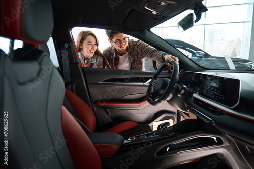 Woman with man look inside of car at dealership choosing suitable vehicle model