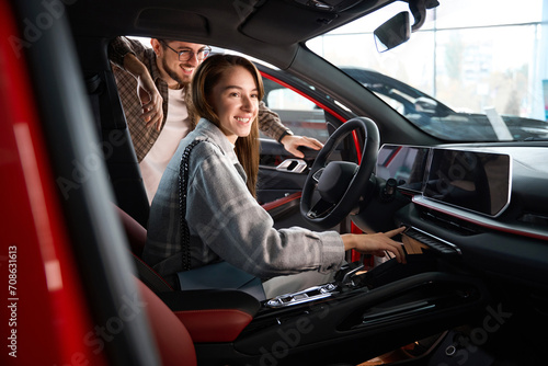 Woman and man choosing model of car in dealership testing model for buying