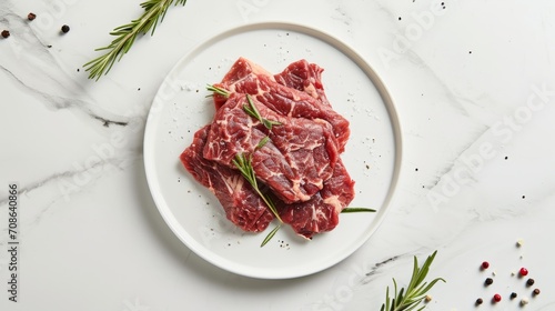 Fresh raw beef steaks garnished with rosemary on a white plate, elegant marble background.