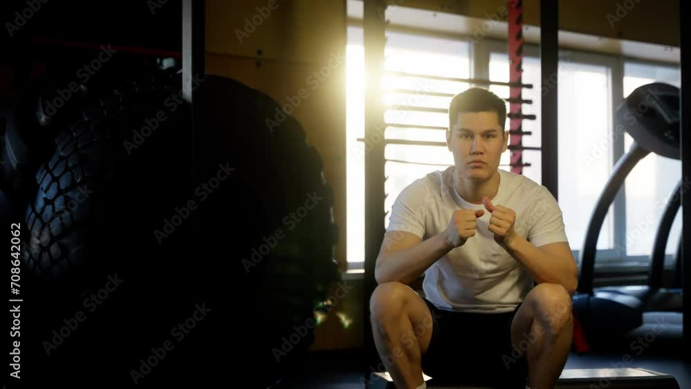 A young man rests thoughtfully in a gym with a large tire, sunlight streaming in A young man rests thoughtfully in a gym with a large tire, sunlight streaming in