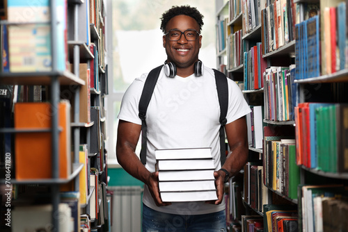Young black man buying new interesting books in bookstore. Cheerful african male student in fashionable clothes with stack of books in university library.  photo
