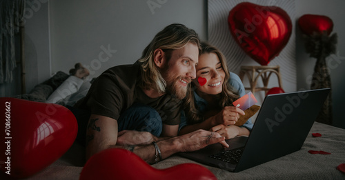 Happy loving couple looking at laptop and using credit card while shopping online at Valentines day