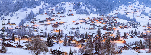 Panorama view of Grindelwald villages with wooden chalets covered with snow in cold winter season at twilght in Swiss Alps