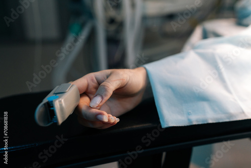 Closeup cropped shot of unrecognizable female hand with pulse oximeter on finger on operating table under anesthesia operating room. Process of medical surgery. Concept of surgery and emergency.