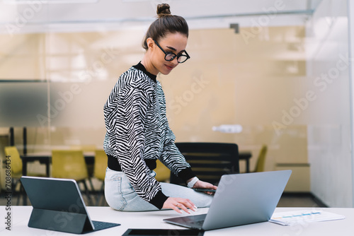 Focused woman working on laptop while sitting on table indoors photo