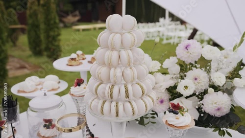 Macaron tower centerpiece on dessert table at garden party, surrounded by cupcakes and pastries. table is adorned with white flowers, providing luxurious and elegant backdrop wedding or high-end event