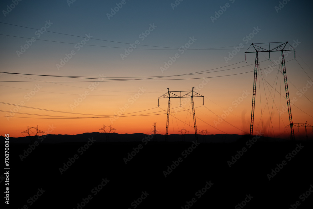 Electric poles and lines over farmland at sunset