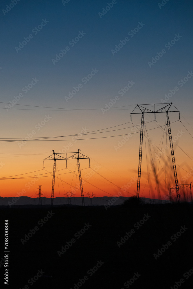 Electric poles and lines over farmland at sunset