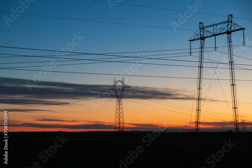 Electric poles and lines over farmland at sunset