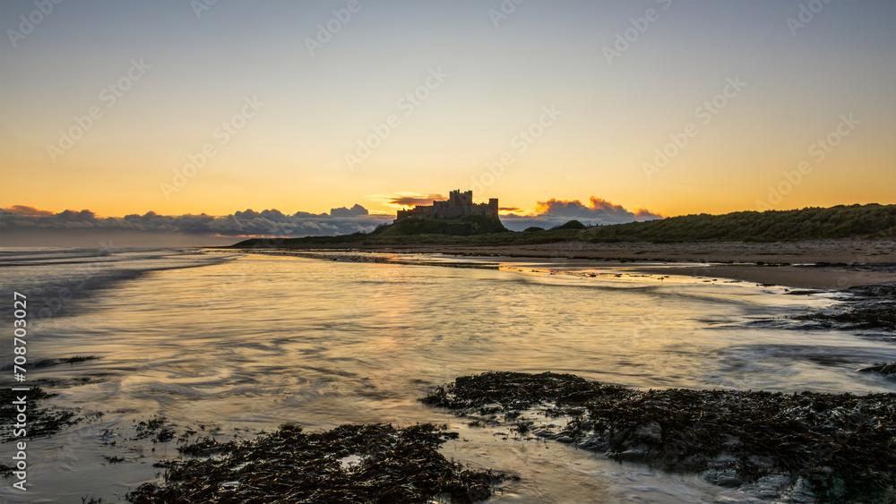 Beautiful landscape image of Northumberland beach in Northern England during Winter dawn with deep orange sky