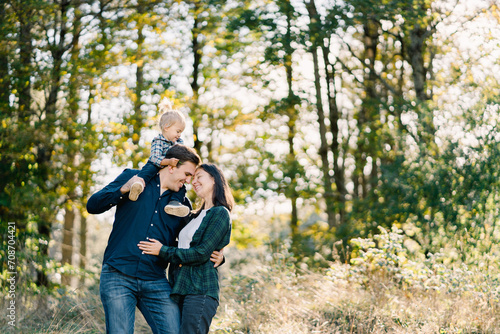 Dad with a little girl on his shoulders hugs mom touching her forehead