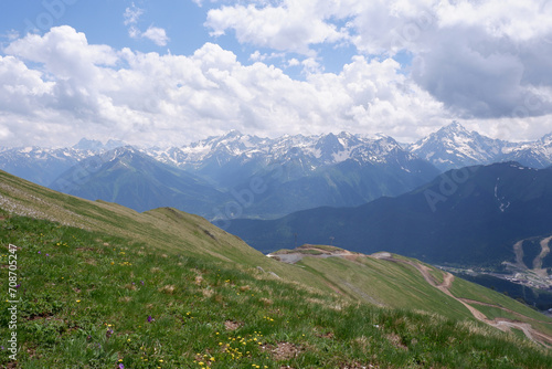 View of an idyllic mountain scenery in the Alps with fresh green meadows blooming on a beautiful sunny day, snow-capped mountains in the distance