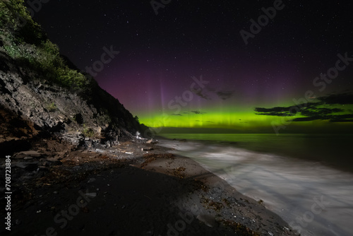 vue sur une plage la nuit avec la lumière d'une aurore boréale qui danse dans le ciel en été