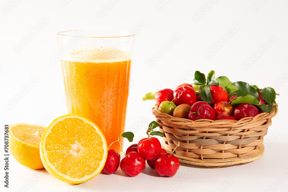 Fresh Organic Acerola and Orange Juice in a glass cup with half orange and acerola berries inside a wood basket in a white clean studio photo in front view Fresh Organic Acerola and Orange Juice in a glass cup with half orange and acerola berries inside a wood basket in a white clean studio photo in front view