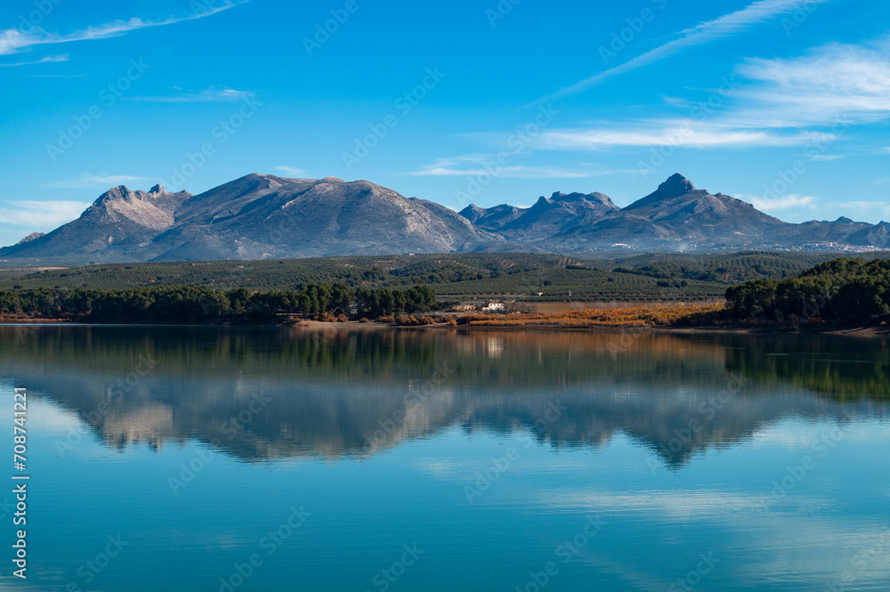 Reflection of mountains and trees in a reservoir in Granada (Spain) on a sunny winter morning