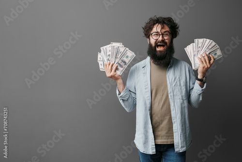 Beaming man with a beard proudly holding up fans of dollar bills, showcasing financial success