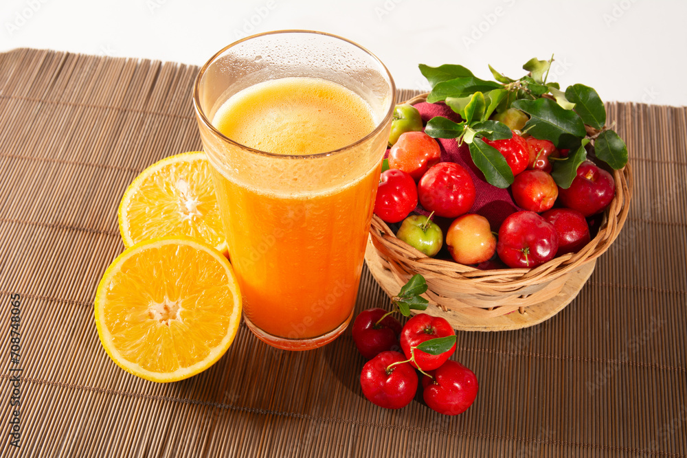 Fresh Organic Acerola and Orange Juice in a glass cup with sliced orange fruit and acerola berries in a bamboo basket in white background in top view Fresh Organic Acerola and Orange Juice in a glass cup with sliced orange fruit and acerola berries in a bamboo basket in white background in top view