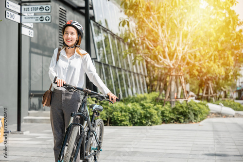 A cheerful Asian businesswoman helmeted and in suit stands with her bicycle symbolizing the modern concept of a joyful business commuter. This image showcases the harmony between work and outdoor fun. © sorapop