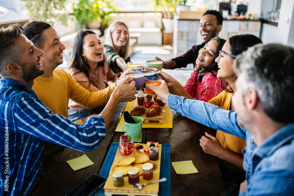 Obraz premium Smiling multiracial group of young people having breakfast together at coffee eatery shop