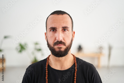 Close-up of Caucasian man with beard looking at camera. Portrait of middle-aged guy concentrating with japa mala necklace indoors. Concept of male wellness, body care, yoga and mental health. photo