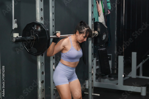 Strong girl with the bar on her shoulders ready to do squats in the gym.