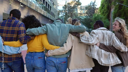 Rear view of diverse people hugging each outdoors. United millennial friends walking together moving away from the camera at city street. Diversity, community and friendship concept.
