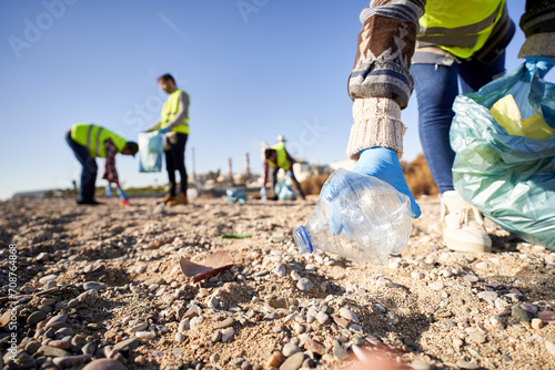 Group of cleanup volunteers cleaning up waste in nature and holding a garbage bag trash. Close up of activist hand picking up a plastic bottle. Concept of environmental protection.