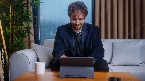 Young professional trader and stockbroker follows the current stock market on his tablet computer while sitting at home on the sofa	 photo