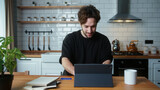 Happy curly hair man sitting in kitchen, using app with tablet computer, surfing on internet	

