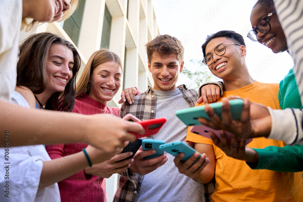 Group of multiracial generation z young smile cheerful people playing funny videos game on a smart phone they holding in their hands. Friends having fun together using social on mobile cell outdoor