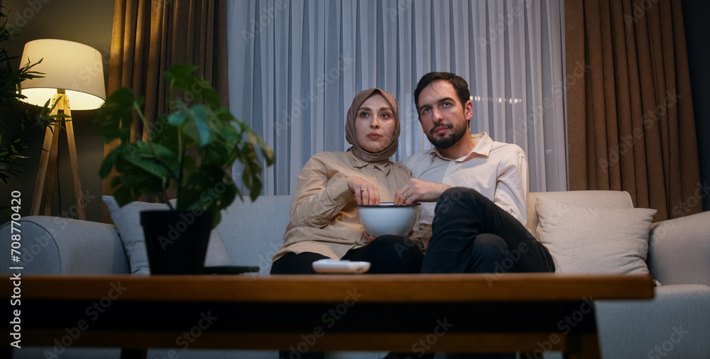 Young married couple watching tv, movies on subscription streaming service in relax living room with popcorn at home at night
Young married couple watching tv, movies on subscription streaming service in relax living room with popcorn at home at night