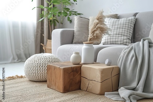Creative composition of stylish modern spacious living room with grey sofa, wooden cubes, pillows, plaid, carpet, white vases and small personal accesories.