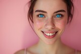 Close-up studio portrait of a young woman with bright blue eyes, smiling, isolated on a soft pink background
