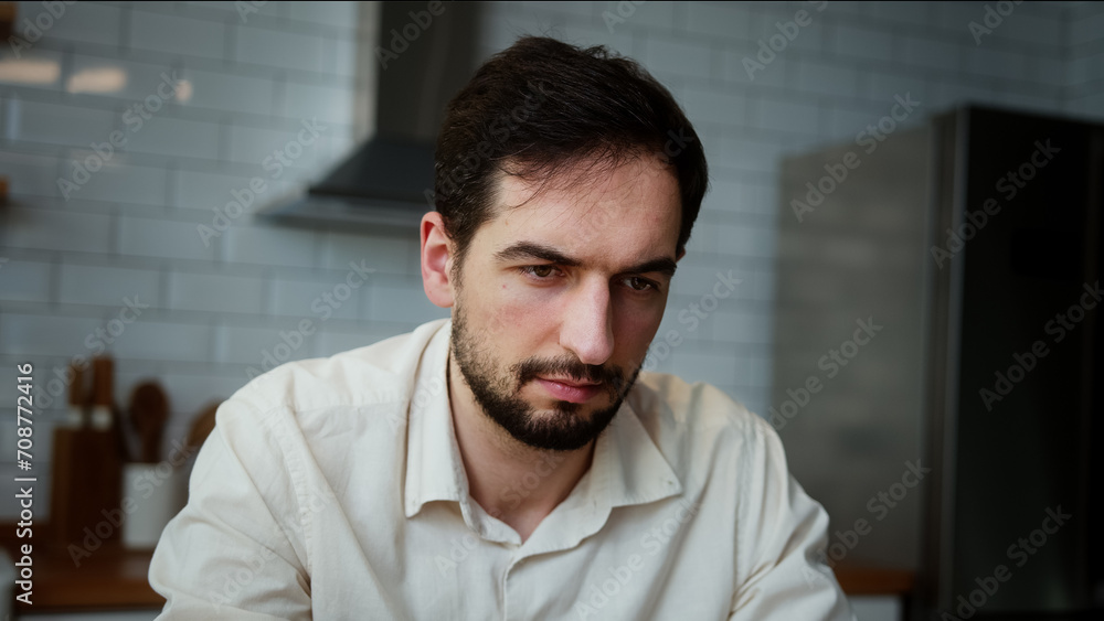 Close up of young bored man sitting at home in the kitchen, spending time on the laptop, surfing internet Close up of young bored man sitting at home in the kitchen, spending time on the laptop, surfing internet