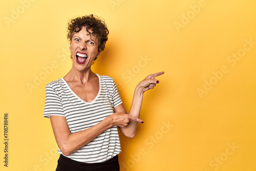 Mid-aged caucasian woman on vibrant yellow pointing with forefingers to a copy space, expressing excitement and desire.