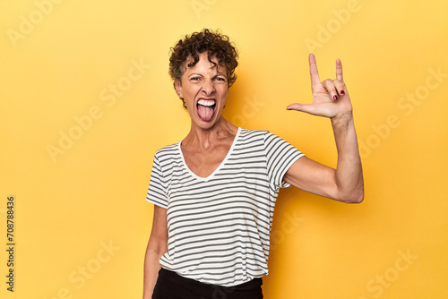 Mid-aged caucasian woman on vibrant yellow showing a horns gesture as a revolution concept. photo