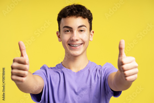 Smiling handsome boy with dental braces wearing stylish casual purple t shirt showing thumbs up © Maria Vitkovska