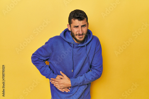 Young Hispanic man on yellow background having a liver pain, stomach ache.