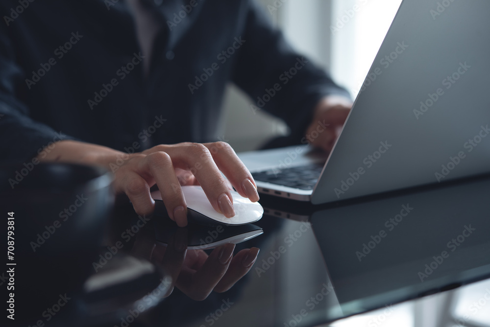 Woman hand clicking wireless mouse on office table. Business woman working on laptop computer and using wireless mouse, browsing the internet, searching the information - obrazy, fototapety, plakaty 
