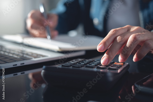 Close up business woman using calculator to calculate financial report and working on laptop computer, calculate expenses, business finance and investment, budget management photo