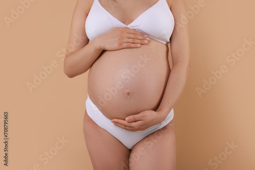 Pregnant woman in stylish comfortable underwear on beige background, closeup