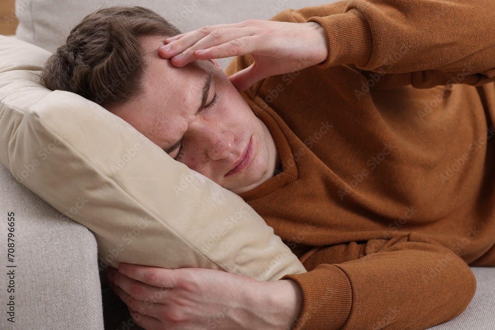 Sad man suffering from headache on sofa indoors Sad man suffering from headache on sofa indoors