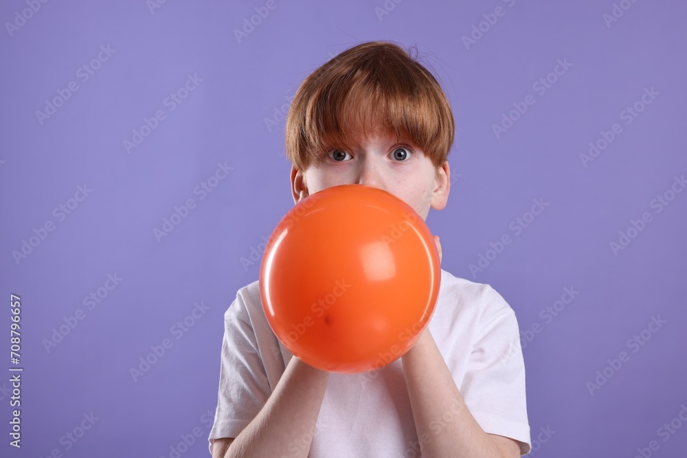 Boy inflating orange balloon on violet background Boy inflating orange balloon on violet background