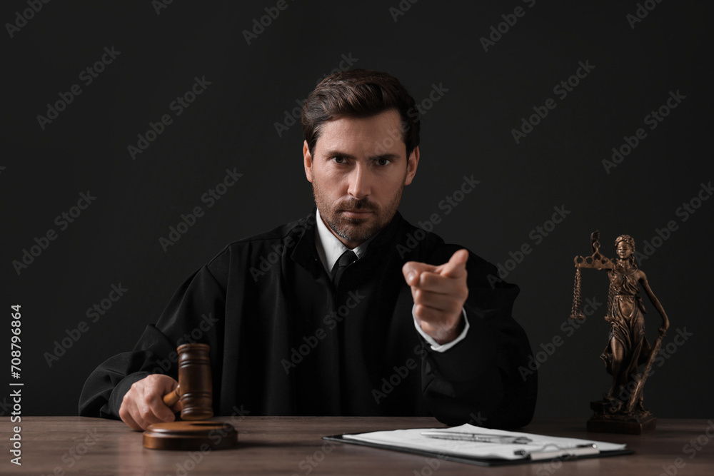 Judge with gavel pointing at wooden table against black background Judge with gavel pointing at wooden table against black background