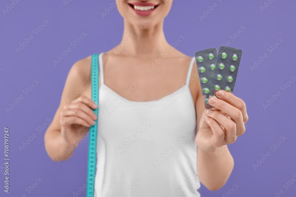 Woman with pills and measuring tape on purple background, closeup. Weight loss Woman with pills and measuring tape on purple background, closeup. Weight loss