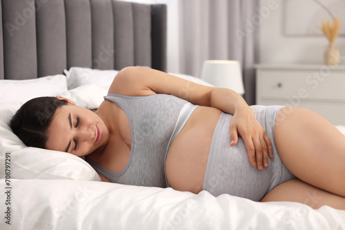 Beautiful pregnant woman in comfortable maternity underwear lying on bed at home