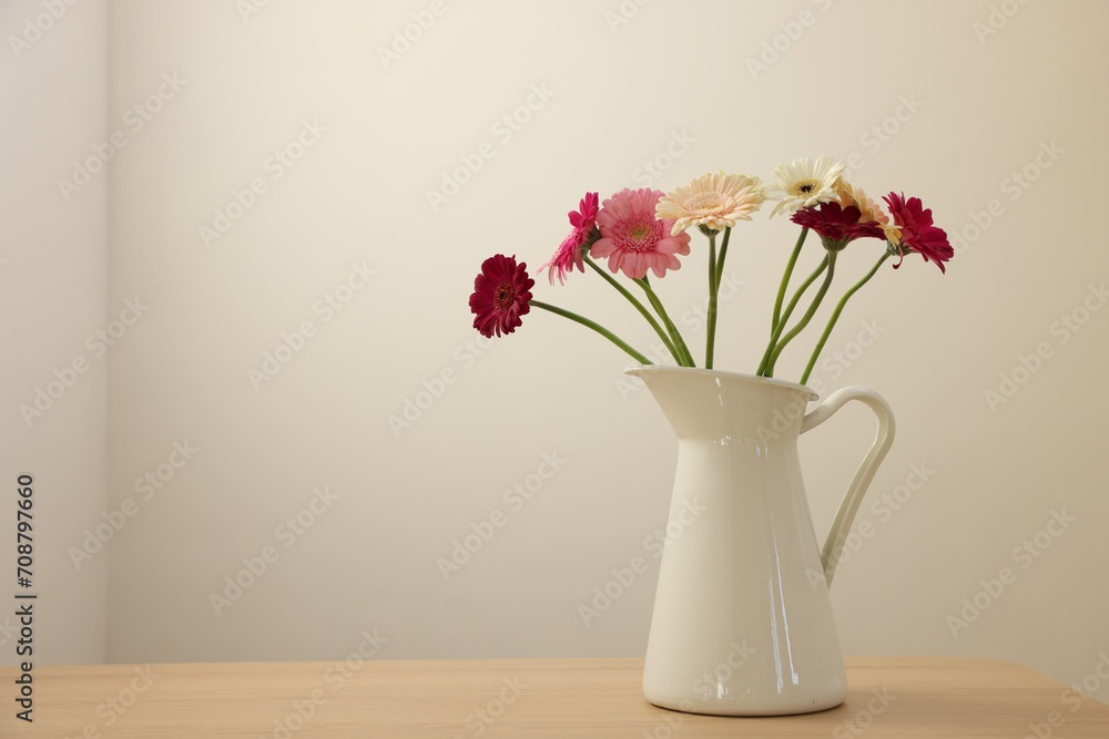 Fototapeta premium Jug with beautiful gerbera flowers on wooden table. Space for text